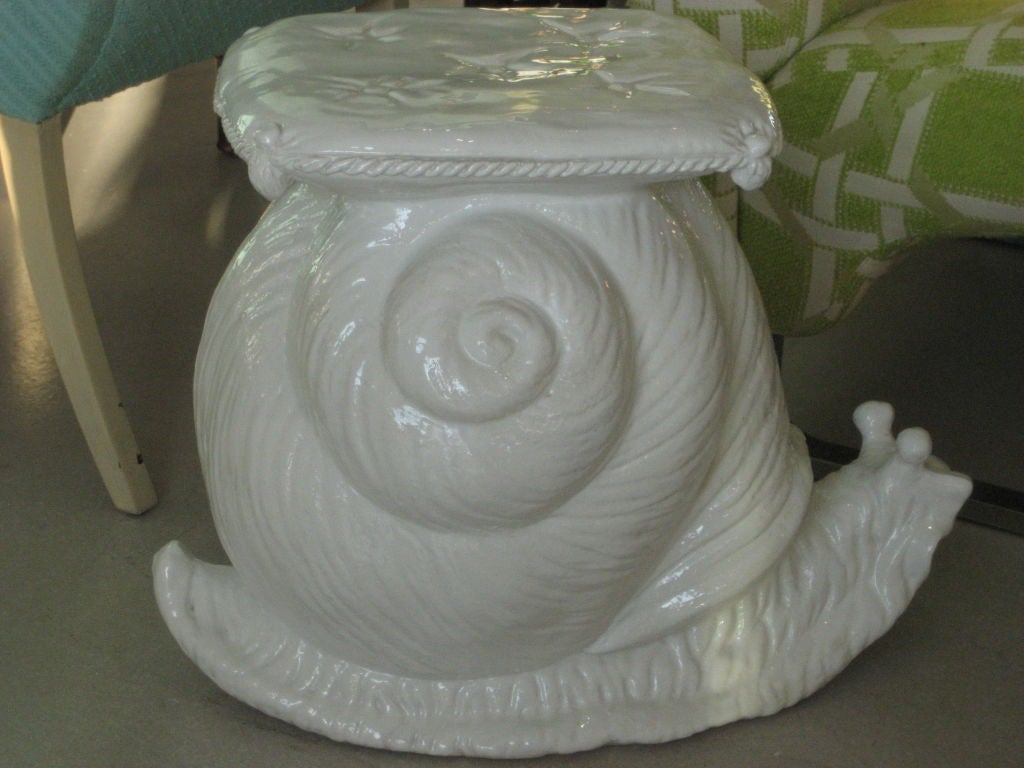 White glazed terra cotta garden seat in the form of a snail. The snail has a cushion on its shell.