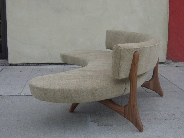 A biomorphic walnut sofa after Vladimir Kagan with curved backrest and a floating platform seat set on sculptural carved legs which blend seamlessly into the support for the back.