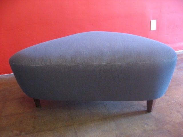Triangular ottoman which has been recovered in grey fabric.