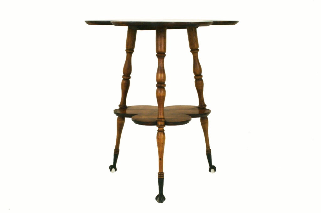 a whimsical two tier table constructed entirely of maple and having two tiers both in the shape of three-leaf clovers, the turned legs connecting the two tiers and continuing to iron and glass ball and claw feet