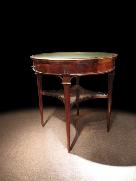 Handsome Louis XVI mahogany bouillotte table with brass enrichments. The circular green tooled leather top surrounded by a brass molded trim. The frieze with two drawers and two leather lined pull out slides which originally would hold the