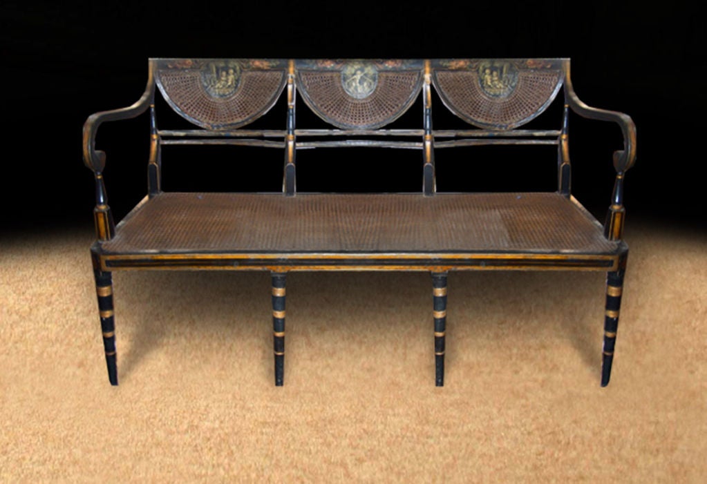 Elegant Regency painted settee, the black lacquered frame nicely trimmed with gold lines. Note the grisaille painted plaques, depicting putti playing, each centered on three half round caned crest rail and back supports. The scrolled arms flank a