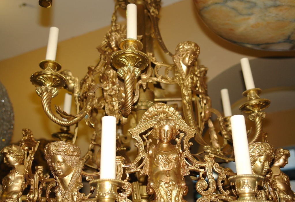 A very large 1920's French, three-tiered neoclassic style chandelier with maiden's masks and 36 lights. Gilt bronze with original patina. The body with scrolling foliage motif.