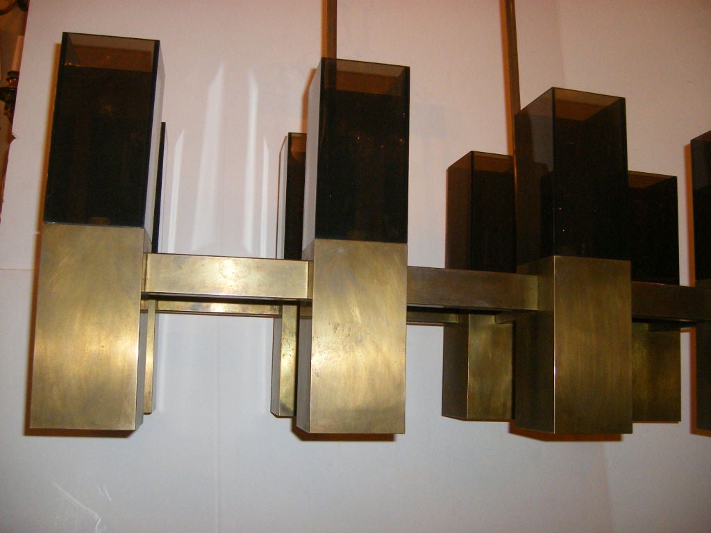 A 1970s patinated bronze light fixture with original patina. The horizontal chandelier has smoke colored Lucite shades. 16 lights, eight up and eight down. 
Measures: 32