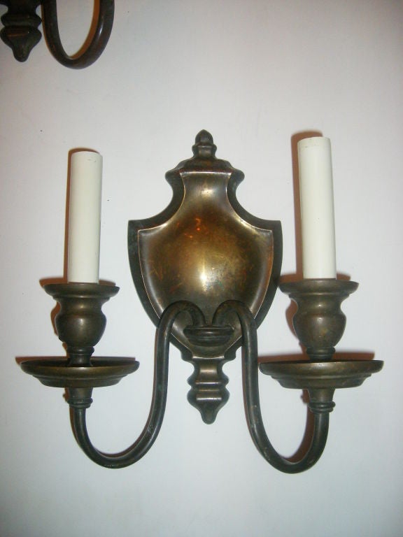 Pareja de apliques Caldwell de dos brazos, de bronce, de hacia 1920, con placa posterior en forma de urna y pátina original. 

Medidas:
Altura: 10
Anchura: 9,5
Profundidad: 4,5