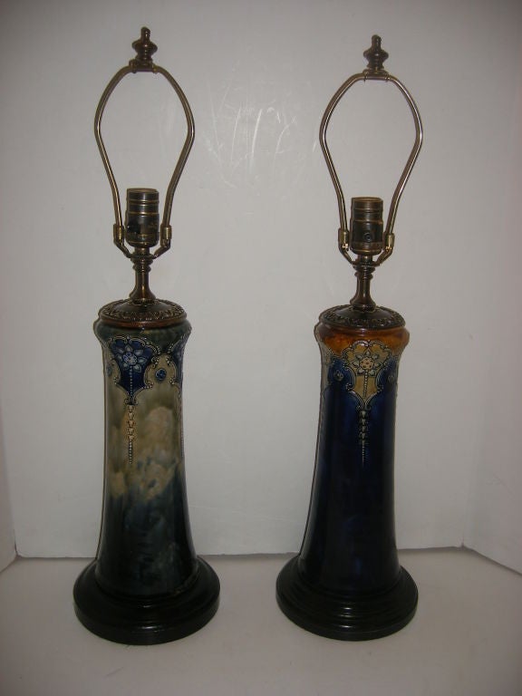 A pair of 1920s Royal Doulton talbe lamps. These are matched, they have blues and pale greens as well as amber colors on the body. Ebonized bases.

15.5