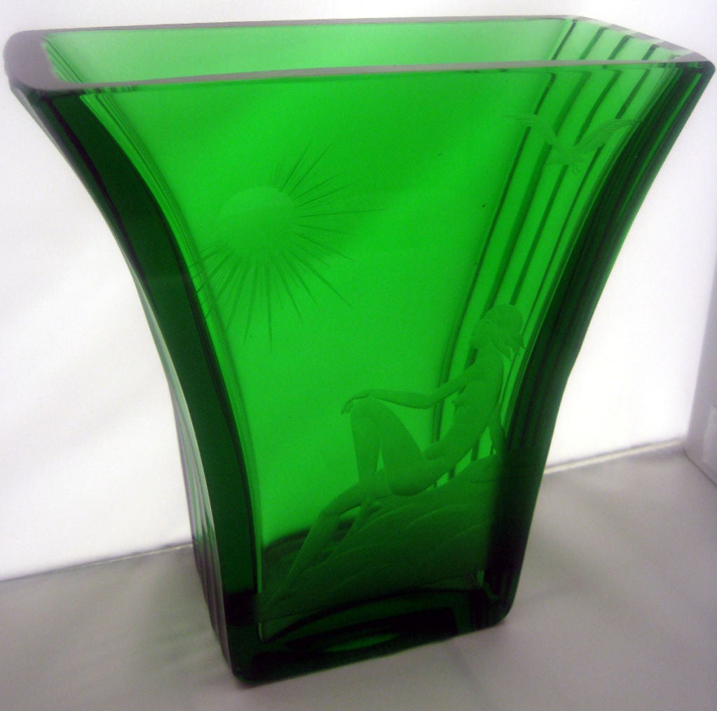 This smart Swedish art deco emerald green mold blown glass vase dates to the 1930’s.  The front panel has a wheel cut nude image of a young lady reclining on a rock and looking at a bright shining sun while a seagull flies overhead.  The vase has