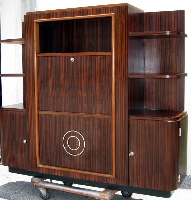 This French art deco secretary is from the 1930’s and is of fine Macassar ebony veneers with sycamore trim and interiors. The fittings are bright nickel plated copper. The center area has an open display shelf at the top. When the front pulls down