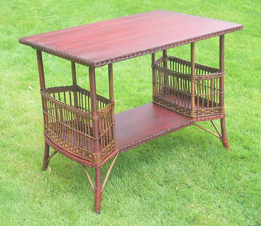 Rectangular wicker side table having large woven magazine pockets on lower shelf.  Oak surfaces with braided border in old red stained finish showing grain. Reeded baskets and supports in a duo-toned light brown finish. Intact Heywood-Wakefield