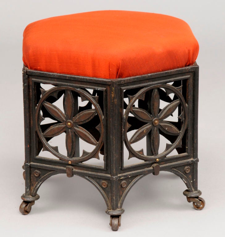 American Gothic Revival hexagonal-shaped cast cast iron stool, with roundels of six petaled flowers and tracery within squares on a base of six cusped arches and legs ending in casters.  Remnants of red paint and gilding still visible. Seat