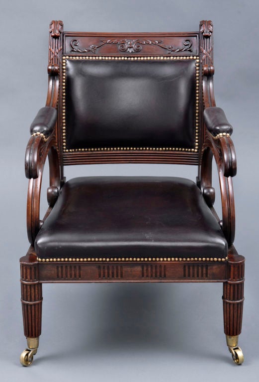 Regency mahogany library armchair, top rail carved with foliate swags, uprights are reeded, arm supports carved in C-scroll shape, seat rail and legs are reeded with ring turnings and raised on brass casters.  Back, seat and arm rests are