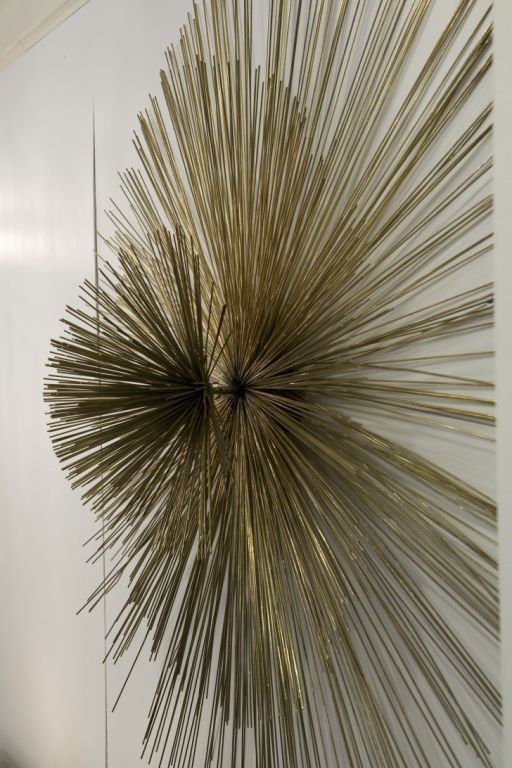 A large Curtis Jere signed gold-toned metallic starburst wall sculpture comprised of three radiating sections of thin metal rods with globe form center.