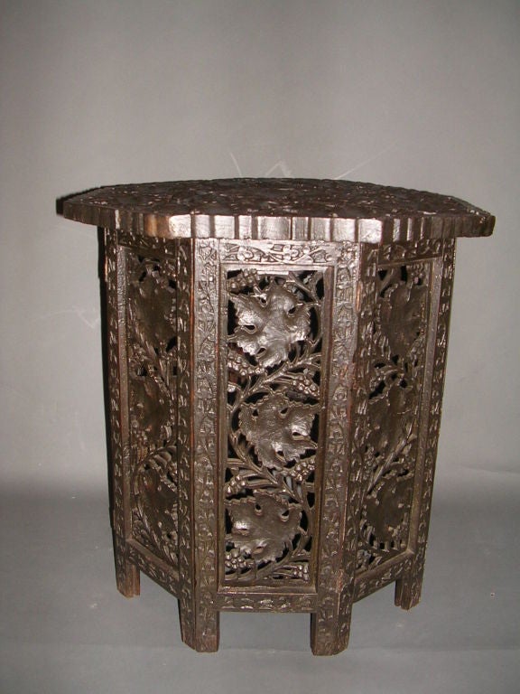 A dark brown late 19th century carved octagonal table the top consisting of leaves, vines and berries resting on a pierced leaf and foliate folding base.