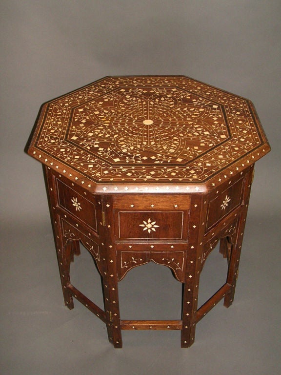 A 19th century Anglo-Indian octagonal ivory inlaid side table the top featuring an eight-sided stylized floral medallion bordered by a band of scrolling foliate deisgn accented in ebony stringing resting on a folding base with small folate inlay and