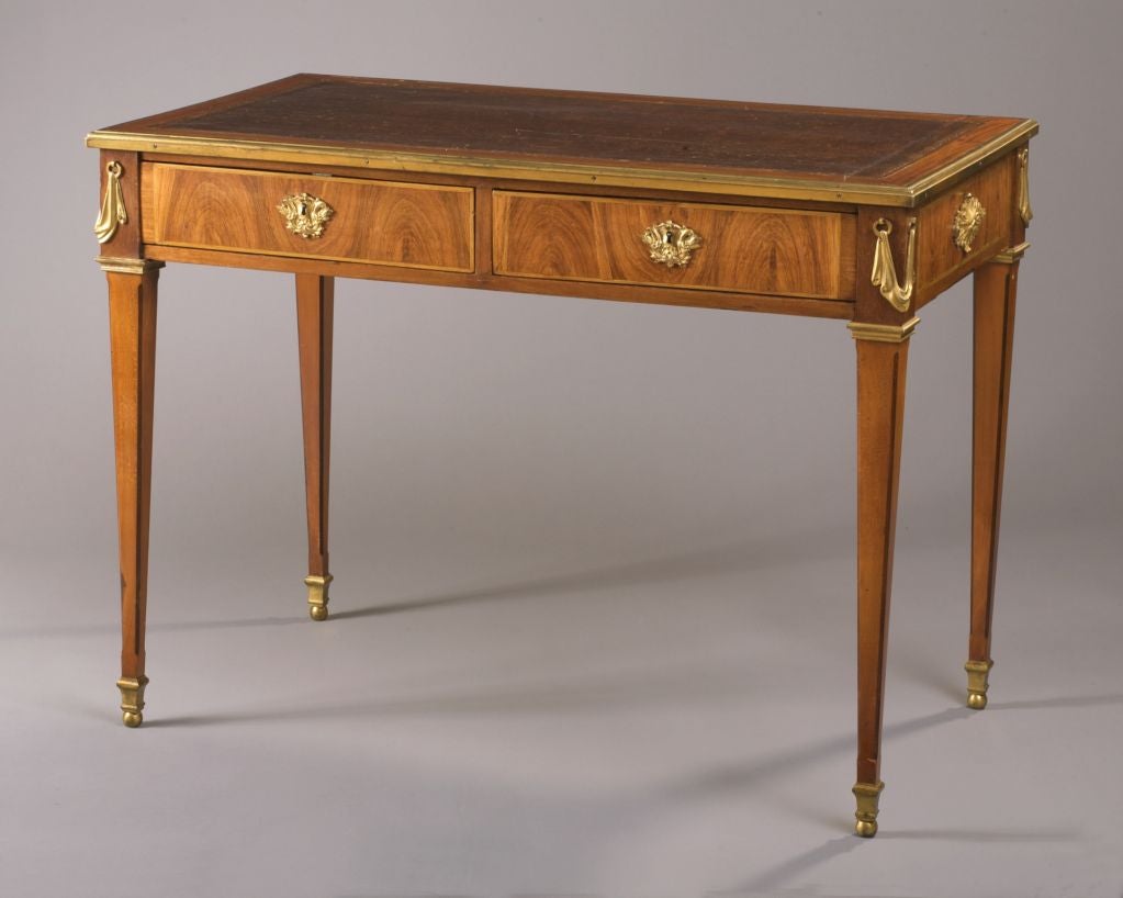 In the style of Montigny (Philippe-Claude Montigny, mai^tre in 1770), the rectangular tooled leather-lined top surrounded with a later ormolu border, above two frieze drawers and simulated drawers to the reverse, the escutcheons in the form of