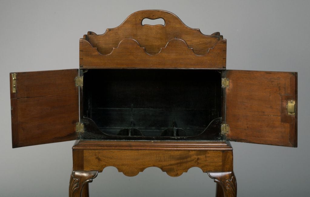 Of rectangular shape, topped by a divided tray with shaped sides over a cupboard with two hinged doors opening to a divided interior and shaped rails, raised on leaf-carved cabriole legs ending in paw feet (with key).  Possibly Irish.