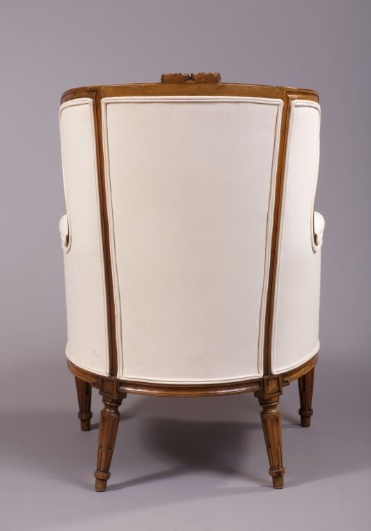 The arched winged backrest carved with a bowknot flanked by padded armrests and a loose seat cushion, the bow fronted seat also carved with a bowknot, raised on round tapering fluted legs.  Made in Lyon, France.