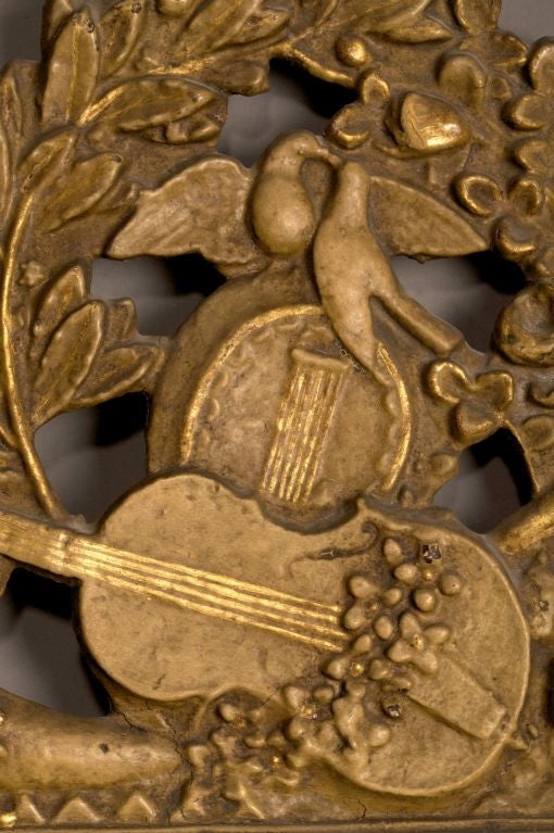 The rectangular original mirror plate within a mirrored border surmounted by a foliate carved crest with birds and musical trophy, each side carved with floral and foliate swags, all above a pierced and swag carved apron centering fleur-de-lys