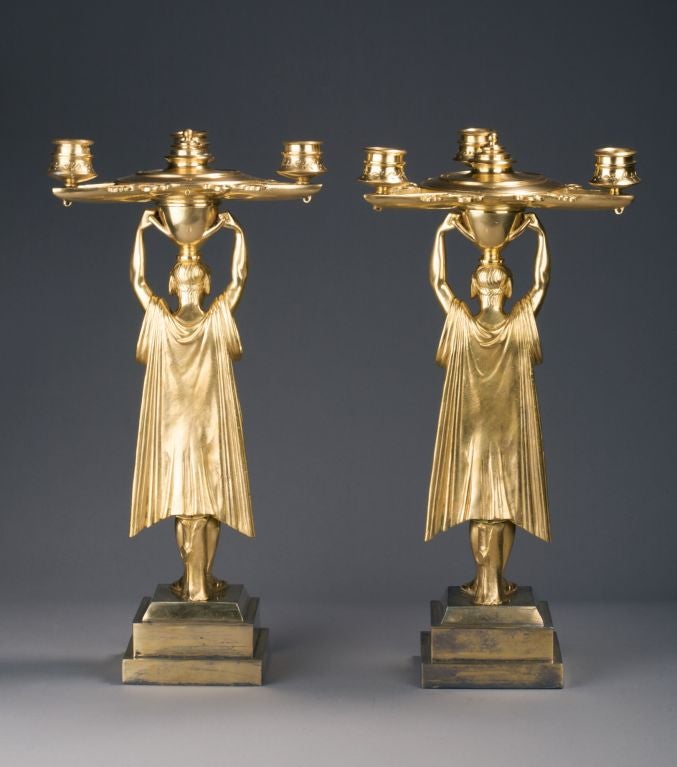 Each Greek style classically draped male figure raising a three-light oil lamp shaped top on a square stepped plinth.