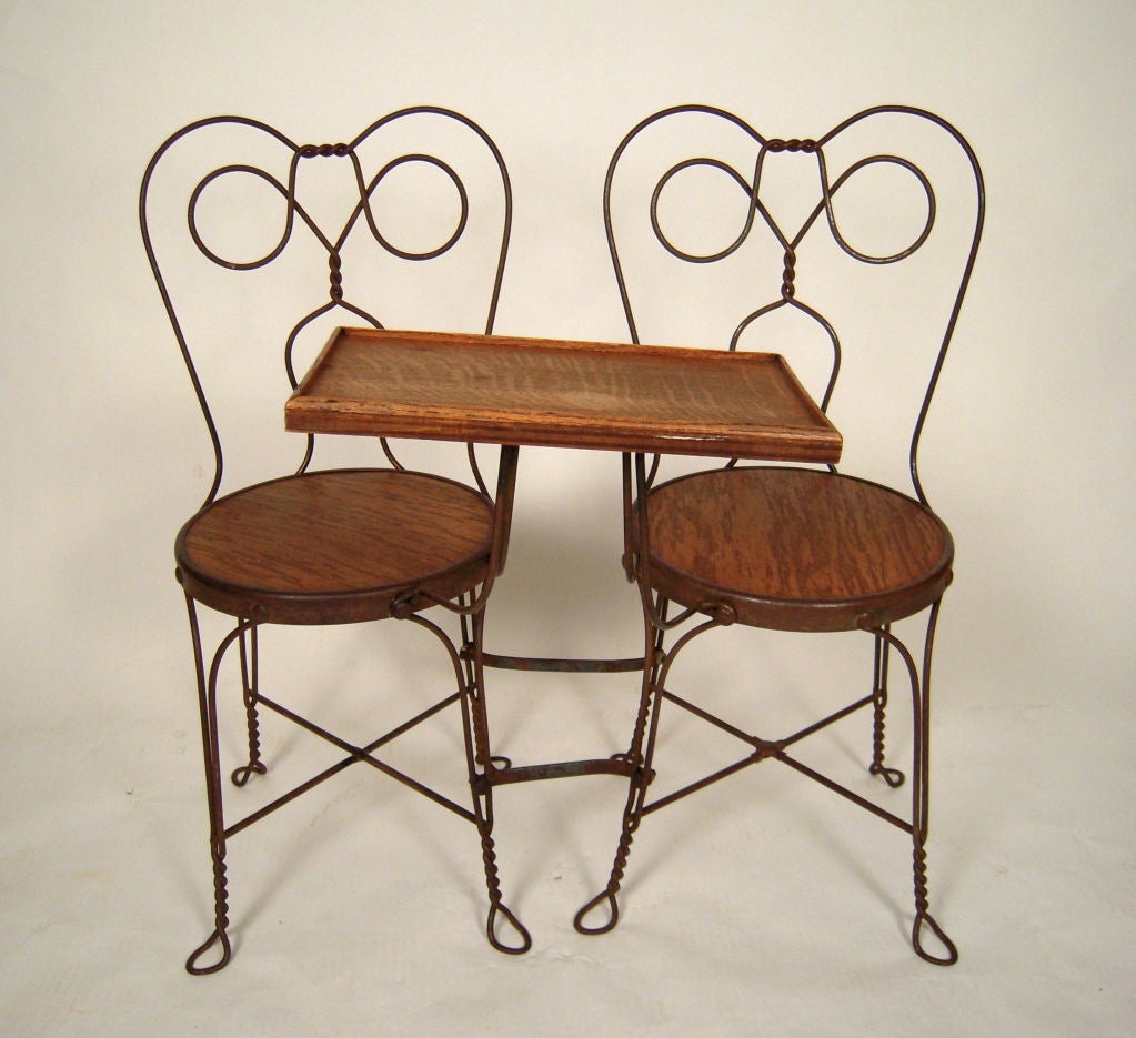 An unusual antique ice cream parlor double seater with attached table, the chairs made from twisted steel, of typical form, the chair seats and table in oak. Excellent as a hall piece or in a bedroom as a valet and pocket emptying tray. Or, of