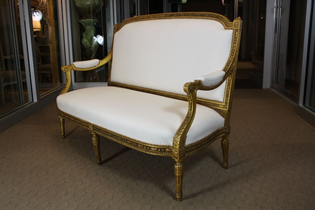 French giltwood canape sofa in the Louis XVI style, with nicely carved neoclassical detailing, including acanthus and bellflower motifs and sunflower joint blocks. Upholstered in heavy white cotton with brass nailheads.