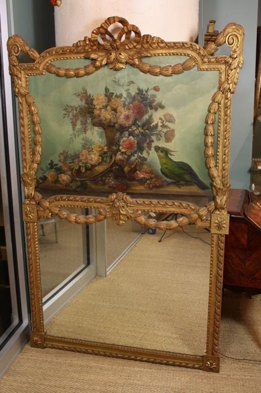 Miroir en bois doré sculpté français avec une peinture de nature morte magnifiquement détaillée de fleurs et d'une urne avec un perroquet vert. Le miroir présente également des éléments néoclassiques joliment sculptés à la main, notamment des