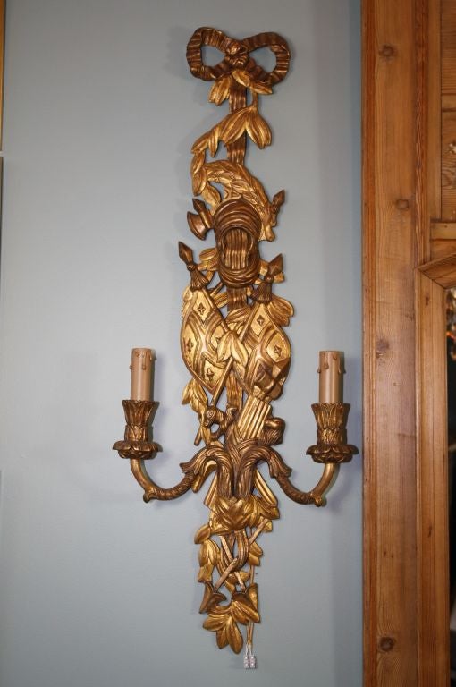 Pair of large Italian giltwood sconces in neoclassical style, with crossed flags, bows and arrows, animals and laurel leaves among other details. Two lights, to be rewired for US with wax candle covers.