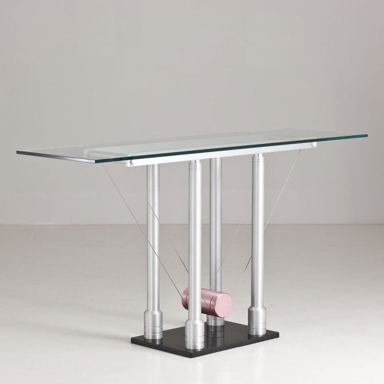 A Memphis style brushed steel console table with a glass top and a wire suspended pale pink cylinder in the centre of the console. All set on a black base. 1980s.
