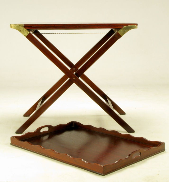 Butler tray table, with folding X-base, in restored burnt sienna mahogany from Baker Furniture. Two flush panel mahogany butterfly leaves unfold from the center on heavy brass hinges to create a 92