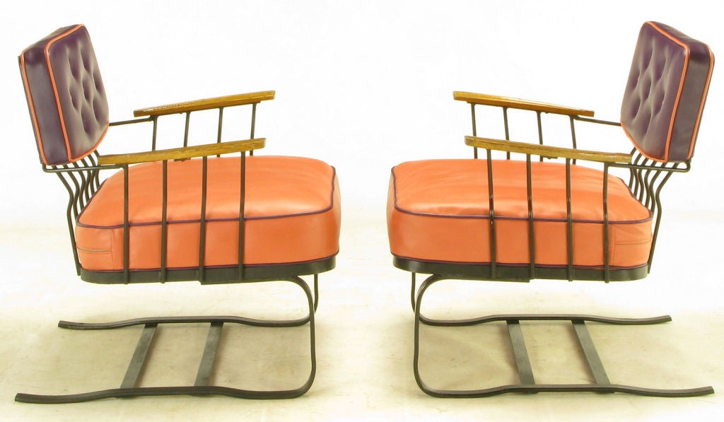 Cantilevered wrought iron, loose-cushion lounge chairs, with carved oak arms and newer button tufted plum and coral high quality vinyl upholstery. Uncommon design from top-quality metal furniture maker, Woodard.