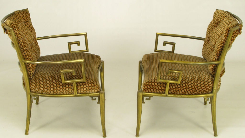 Elegant brass armchairs with Greek key form arms, and decorative brackets to the front and back legs. Geometric patterned brown velvet upholstery is original, as is the mellow brass patina.