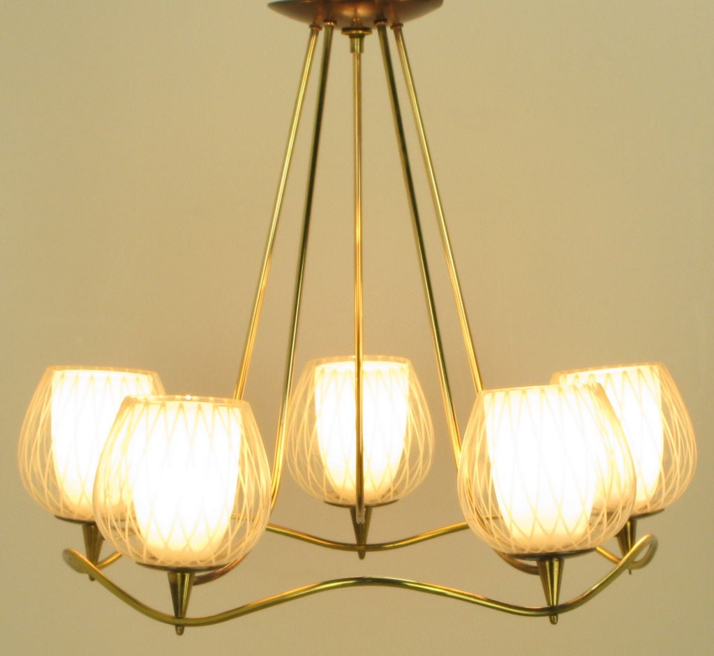 Very well designed chandelier of curvaceous brass rod and two-part etched and milk glass shades. Most likely by Gerald Thurston for Lightolier. Five two part shades consist of a milk glass interior hurricane surrounded by an etched wine glass clear