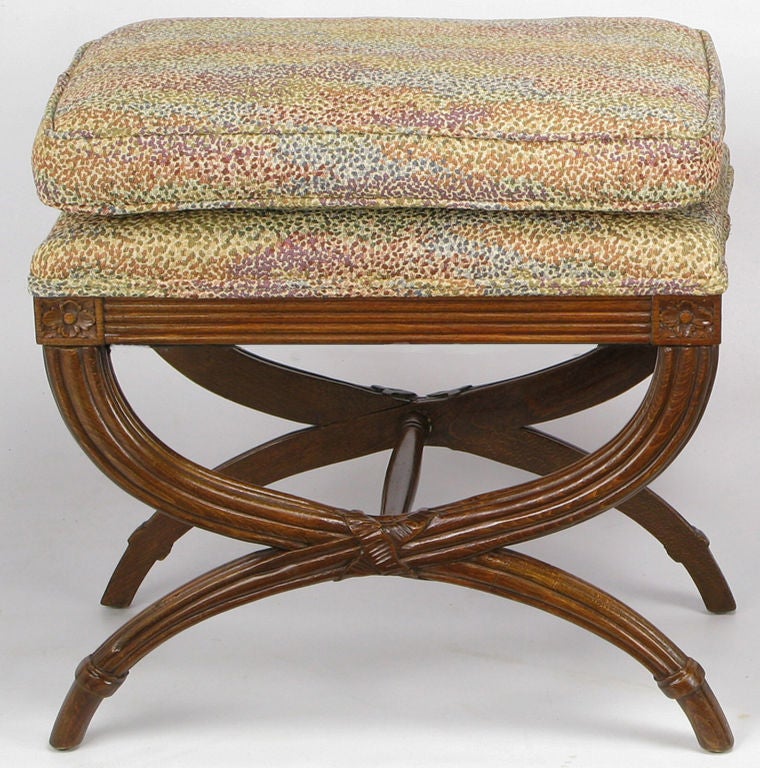 Carved oak curule form benches, with reeded legs, apron, and center cross stretcher.  Detailed with corner rosettes, and linen fold wrap at the intersection of the legs. Abstract polka dot multicolor needlepoint-look upholstery.