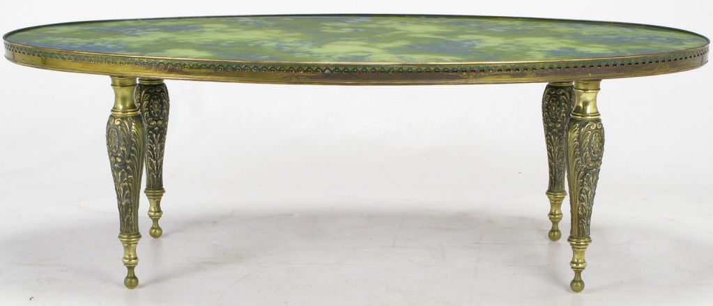 Pierced brass gallery surrounds a reverse painted glass variegated blue and green oval top. Supported by four cast and patinated brass Italian rococo legs.