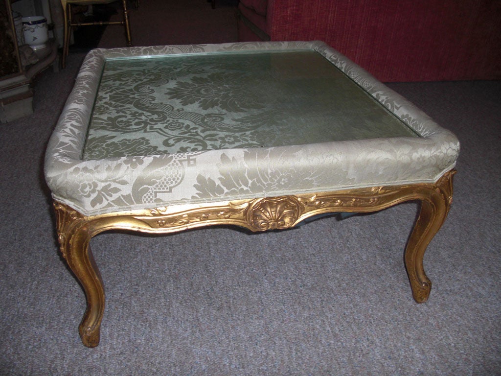 A circa 1860 carved and gilt wood Louis XV style ottoman adapted into a coffee table in the 20th century. You can leave it as a coffee table or it is no problem to reupholster it as an ottoman. Someone went through a lot of expense to have a thick