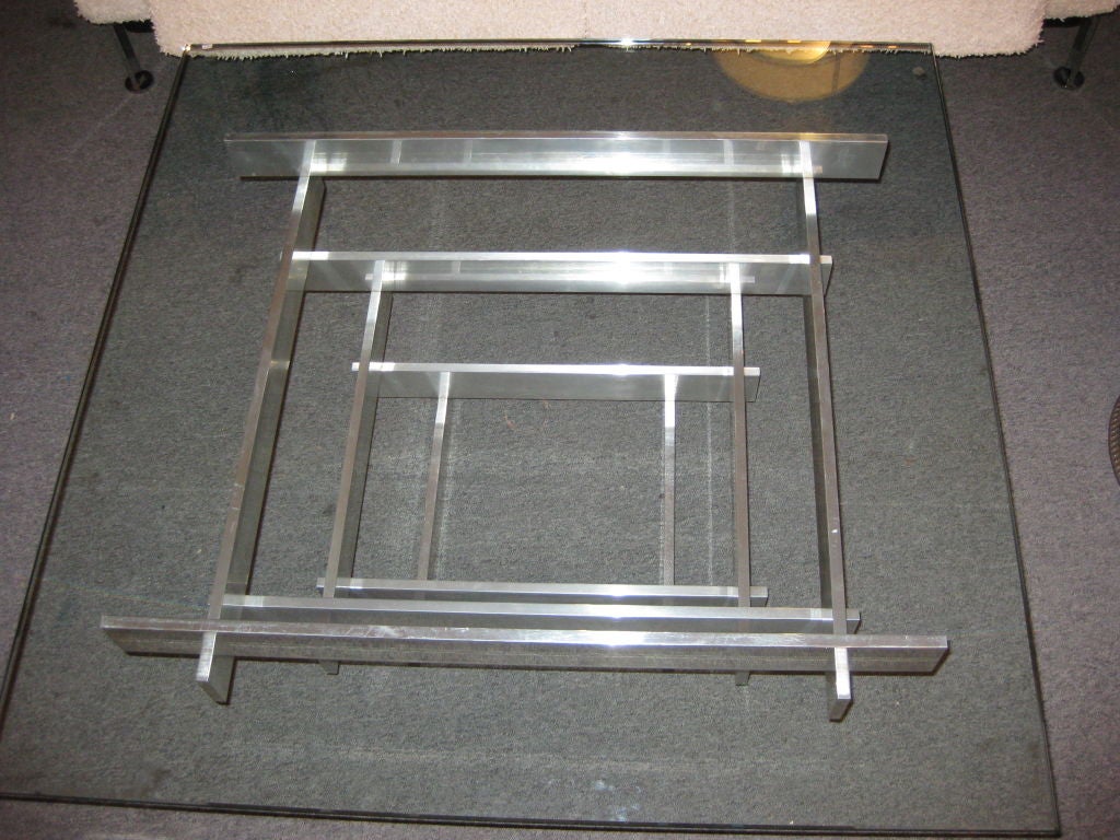 Square glass coffee table with aluminium supports stacked concentrically smaller to larger.