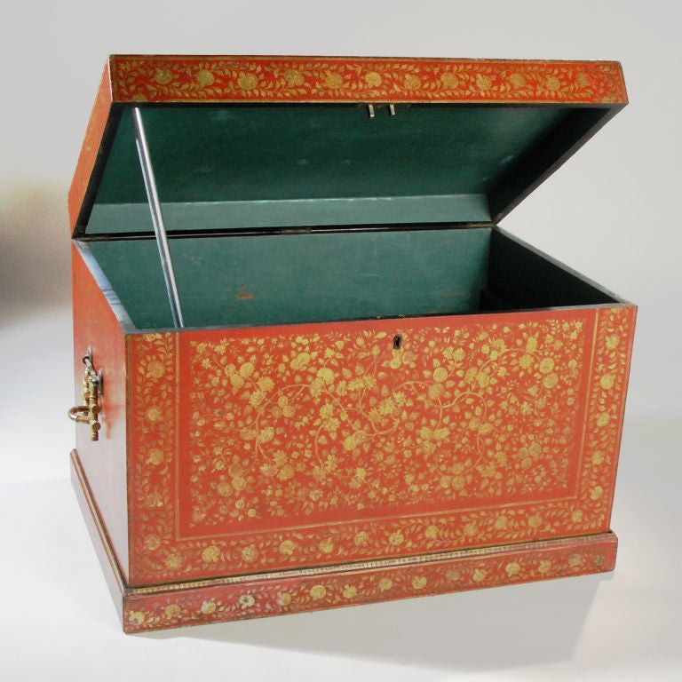 Oversized lacquered trunk in red/orange tones. Painted in gold paisley flower design with distinct bronze handles. Raised on fitted matching wood stand.