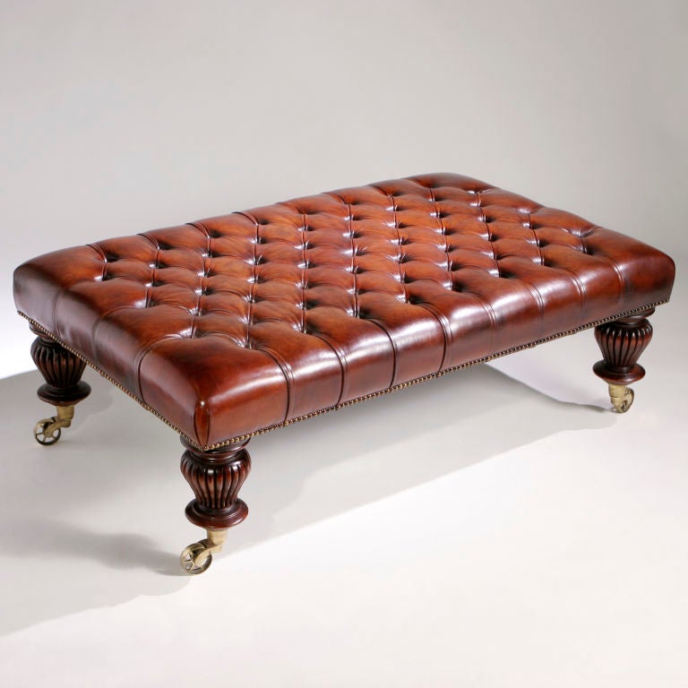 Large deep button tufted leather bench on carved wood legs with artillery brass castor wheels.  Upholstered by an English saddle maker in distressed tobacco brown color leather.  Limited edition re-creation.