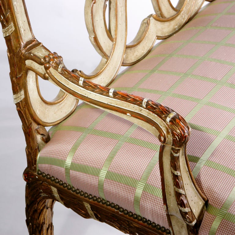 One of a pair of exceptional Italian gilt wood settees with stylized ribbon back in painted finish with gilt detailing.  Twisted ribbon design on top rail carried through to arms, apron and legs.  Upholstered in pale pink and green plaid silk.  Each
