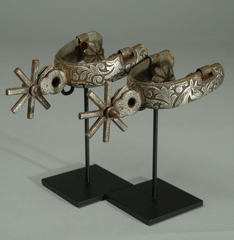 A pair of fancy late 19th century Mexican silver inlaid 'vaquero' spurs with large 2.5 inch, eight point rowels and 3 inch heel-bands. Beautiful silver work throughout. Displayed on a pair of high quality custom stands.<br />
<br />
Dimensions: