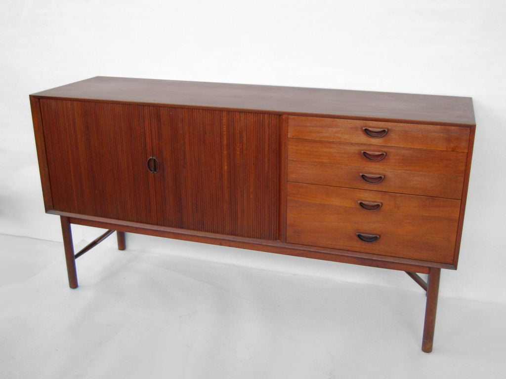Solid teak credenza on high base having 2 tambour doors<br />
and four drawers. Storage space with one adjustable shelf behind tambour. Very nice exposed finger joint construction on cabinet top and sides. Sculpted solid teak handles. Drawers