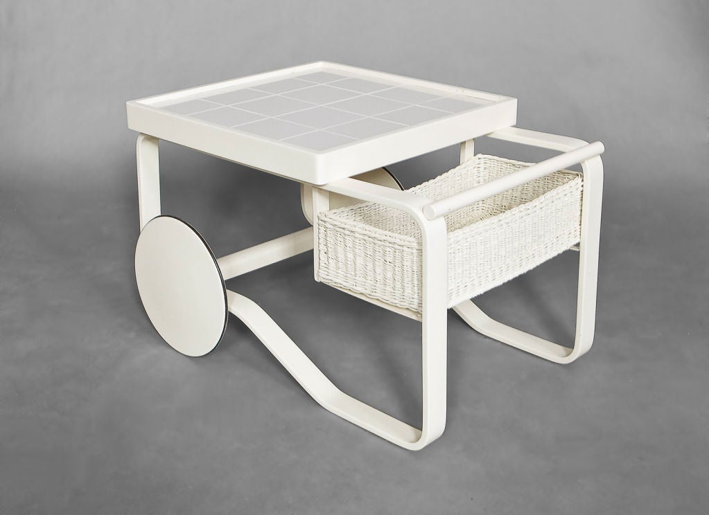 Alvar Aalto tea trolley in white lacquer with tile top<br />
and wicker basket.  Design originally introduced at the 1937 World's Fair in Paris. This production 1960's.