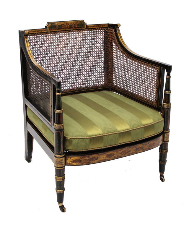 An associated pair of Regency black painted and parcel-gilt decorated caned square-back bergeres with loose cushions back, on <br />
turned tapered legs ending in brass casters.