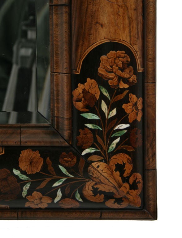 A William and Mary walnut and marquetry cushion mirror with a bevelled rectangular plate, the frame inlaid with panels of bird and loral marquetry incorporating green-stained bone.<br />
Provenance: Glemham Hall, Suffolk