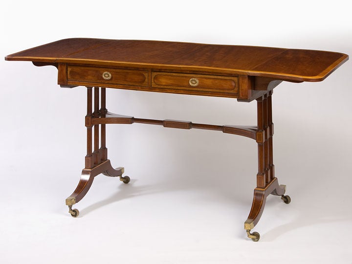 Good English Regency sofa table in mahogany with satinwood<br />
cross-banding having turned end supports with a central stretcher<br />
supported on down-swept legs ending with brass casters.