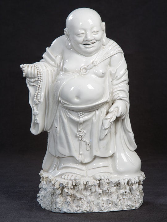 Exquisitely Detailed and Elaborate Blanc de Chine Porcelain Representation of the Mythical Demi-God,  Budai (cloth sack), Carrying his Bag of Gifts in One Hand and a String of Prayer Beads in the Other.  <br />
For an Almost Identical Example in