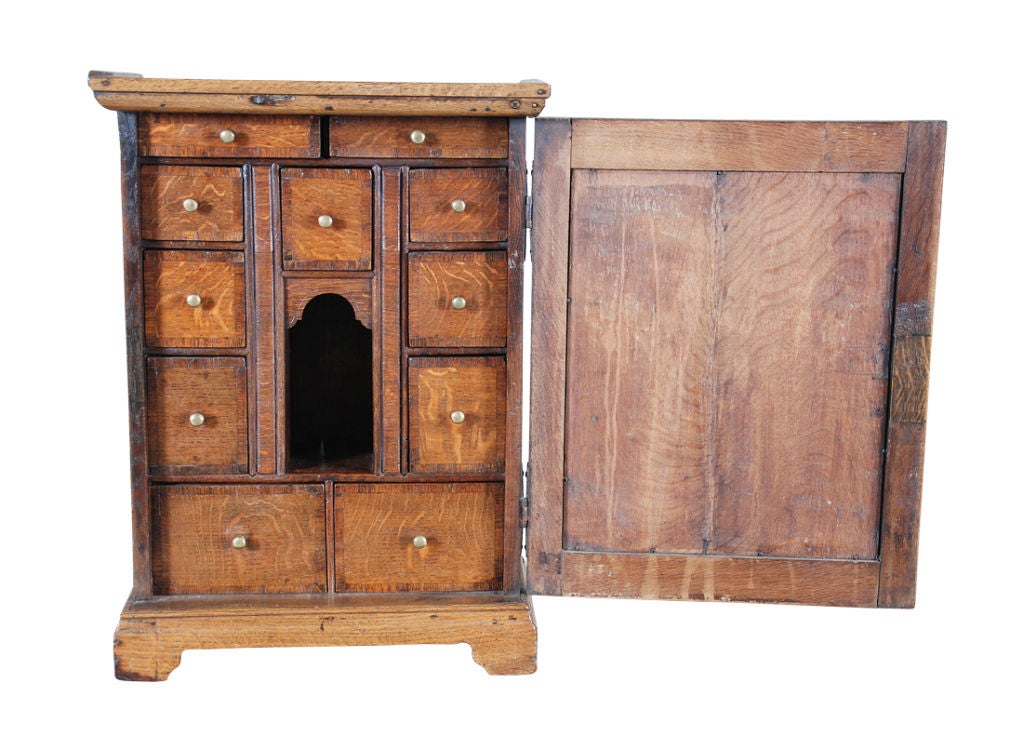 An English oak spice cupboard with cross-banded, paneled door concealing an interior fitted with cross-banded drawers surrounding an arched cubby-hole. Standing on bracket feet.