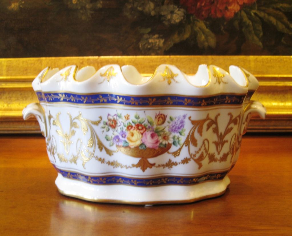 Hand painted Paris porcelain oval fluted cachepot or tureen with a scalloped top edging. It has hand applied gilt scrollwork and floral garlands with a central flower filled footed urn on each side. This decoration is framed inbetween two deep blue