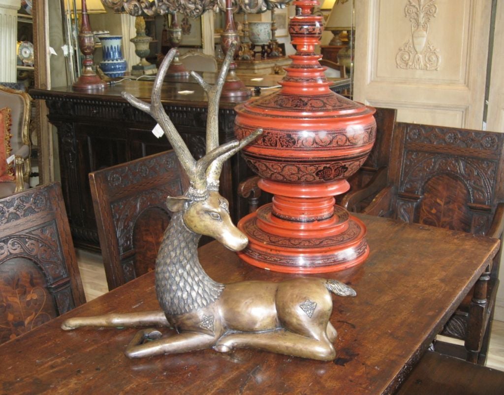 A stylized reclining bronze deer sculpture from Thailand with a rich patina. The horns and fur are highly textured.    Intricate medallion applique designs on the shoulders, haunches and the forehead. Extensive detailing also found at the base of