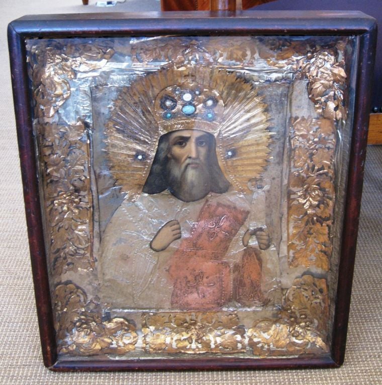 A Russian Icon of Christ in elaborately hand cut foils of copper, gilt and silver. The crown has semi precious stones including pearls, turquoise, and ivory. It is in its original wooden frame or 'Kiot'.